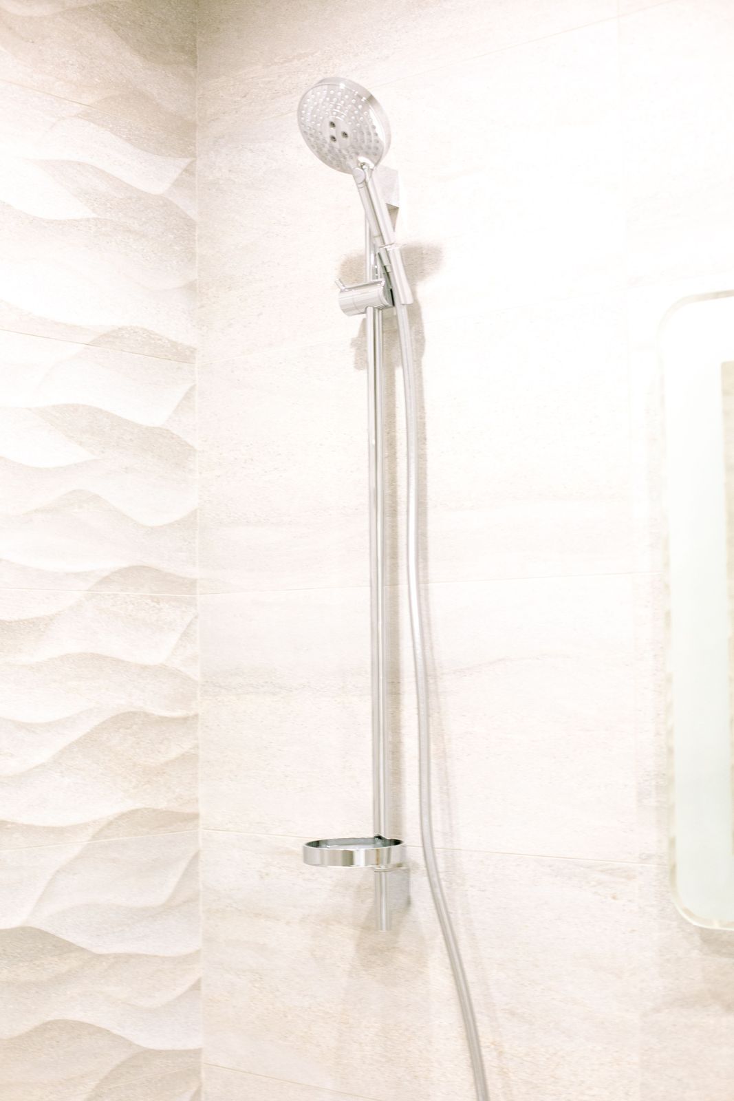 Chrome handheld shower head on a vertical slide rail with a soap dish against textured wave tiles