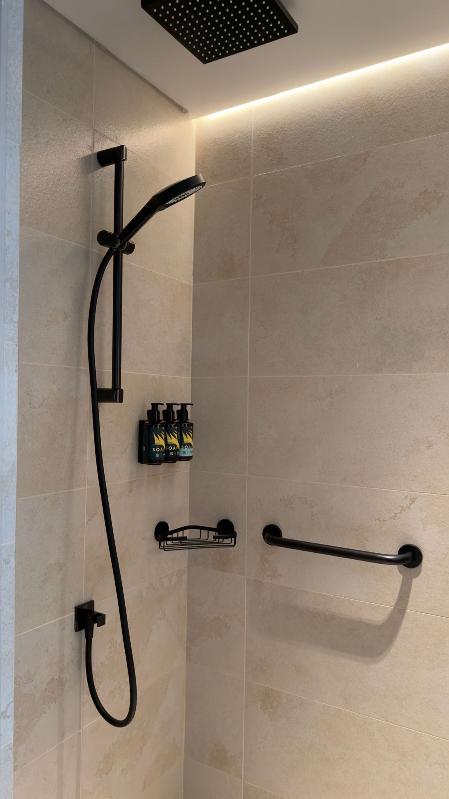 Matte black handheld shower on a slide rail below a square ceiling rain shower in a beige tiled shower
