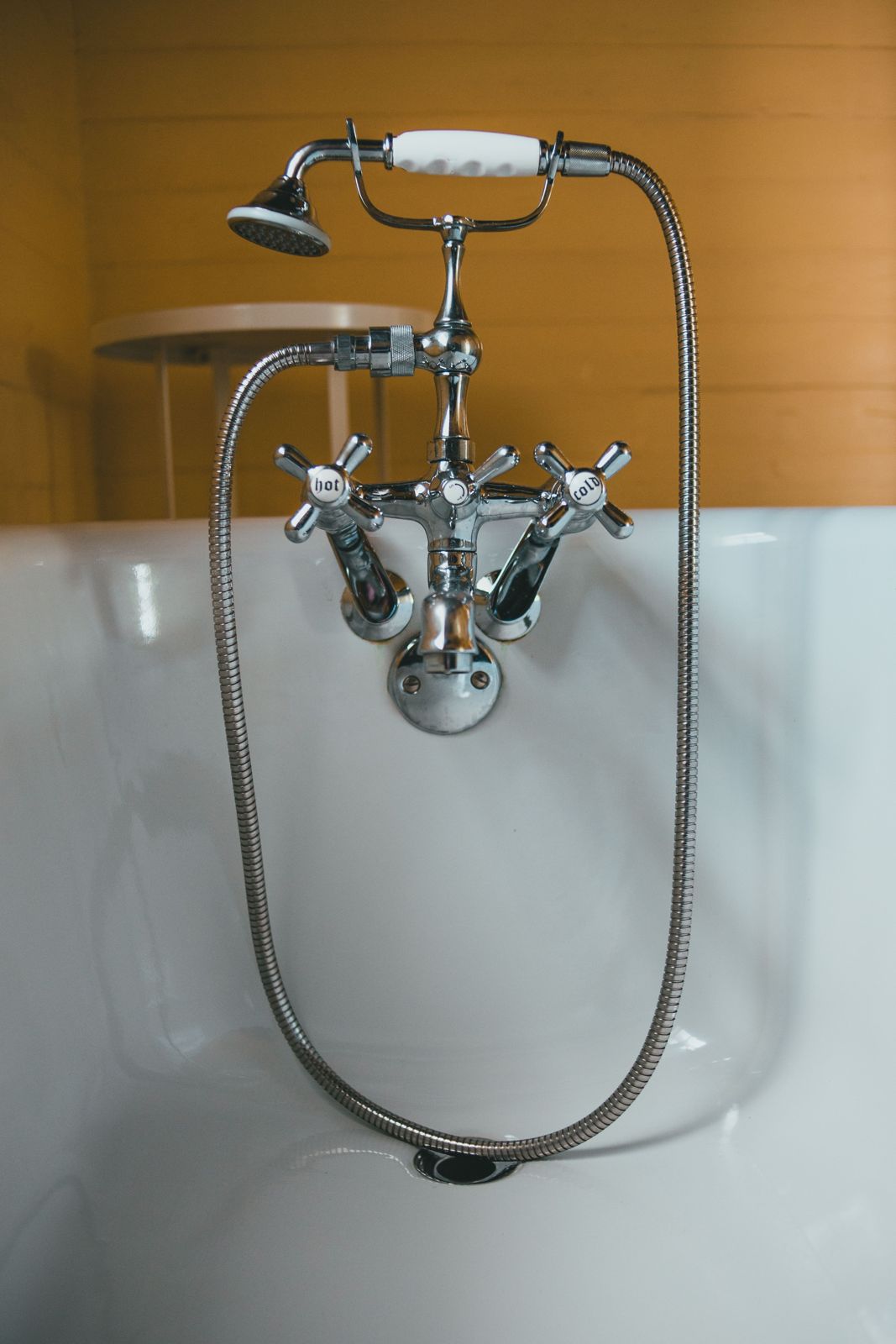 Chrome telephone-style bath shower mixer with hot and cold cross handles and a metal hose on a white tub