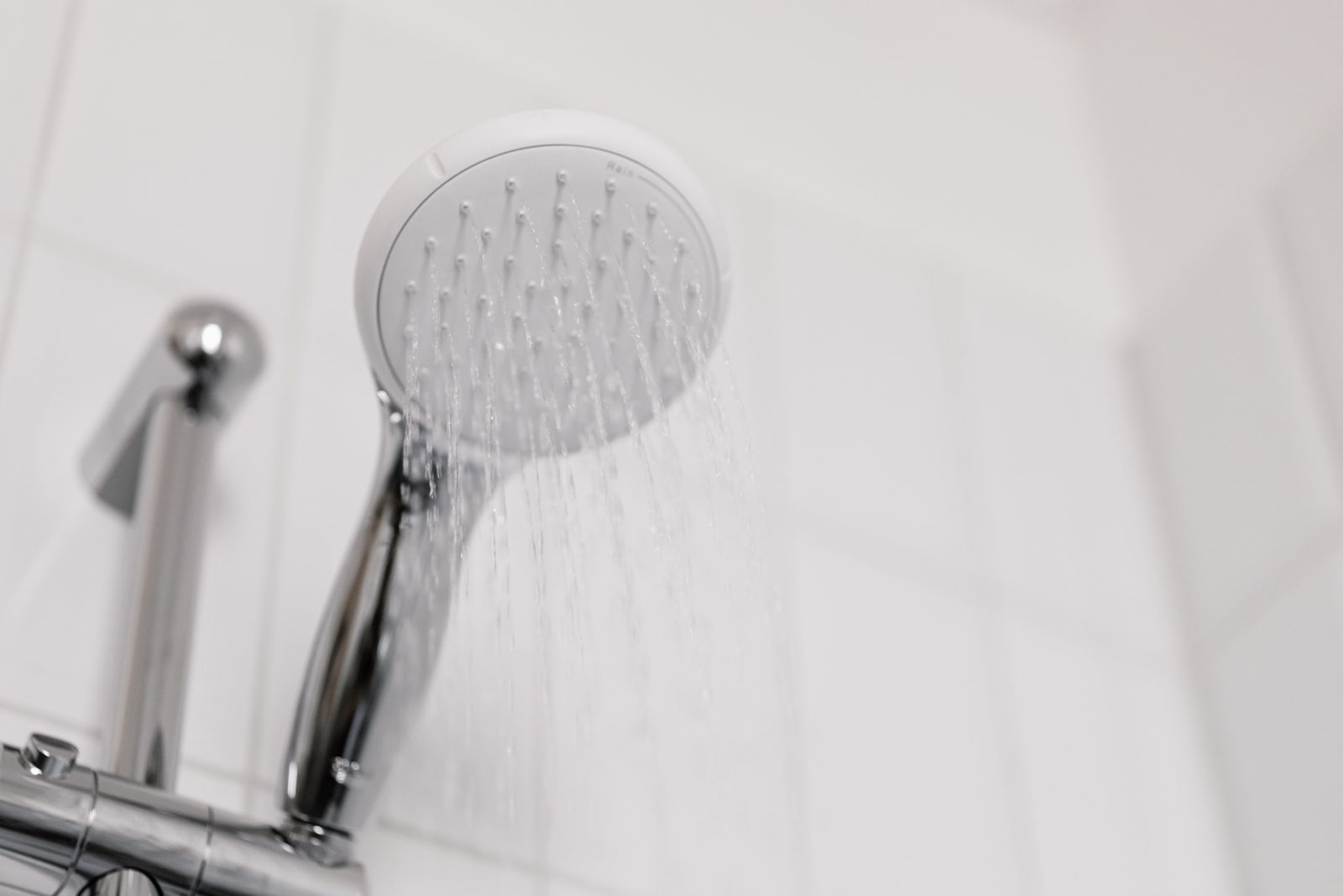 White handheld shower head spraying fine streams of water beside a chrome shower valve